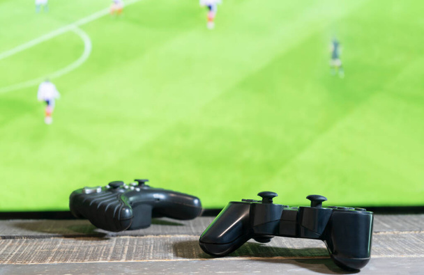 Vista de cerca del controlador de videoconsola de dos juegos con partido de fútbol, televisión de pantalla verde en el fondo.Concepto de juego. - Foto, Imagen
