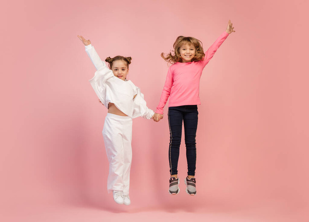 Happy kids, girls isolated on coral pink studio background. Look happy, cheerful, sincere. Copyspace. Childhood, education, emotions concept - Φωτογραφία, εικόνα