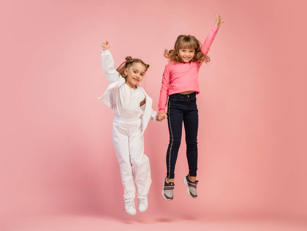 Happy kids, girls isolated on coral pink studio background. Look happy, cheerful, sincere. Copyspace. Childhood, education, emotions concept - 写真・画像