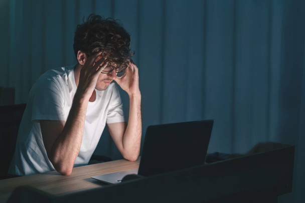 Depressed caucasian man be sleepless losing job and heartbroken at same time sitting alone in front of laptop with low light environment, PTSD Mental health and depression concept. - Foto, imagen