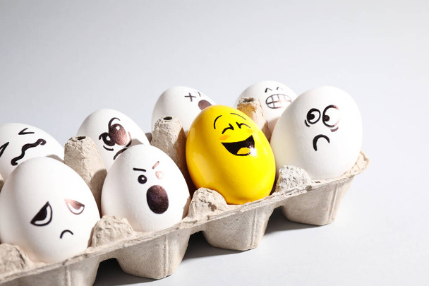 Yellow smiley egg among others with negative emotions in package on light background - Zdjęcie, obraz