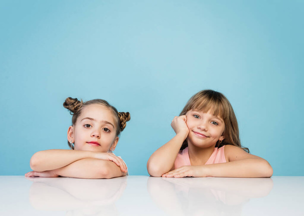 Happy kids, girls isolated on blue studio background. Look happy, cheerful, sincere. Copyspace. Childhood, education, emotions concept - Photo, Image