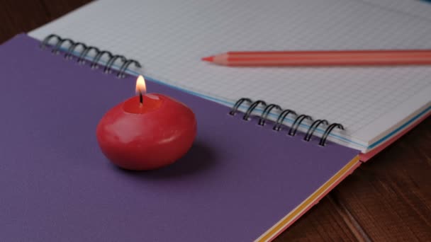 Μικρό κόκκινο στρογγυλό κερί καίει δίπλα σε ένα notebook close-up 4k βίντεο - Πλάνα, βίντεο