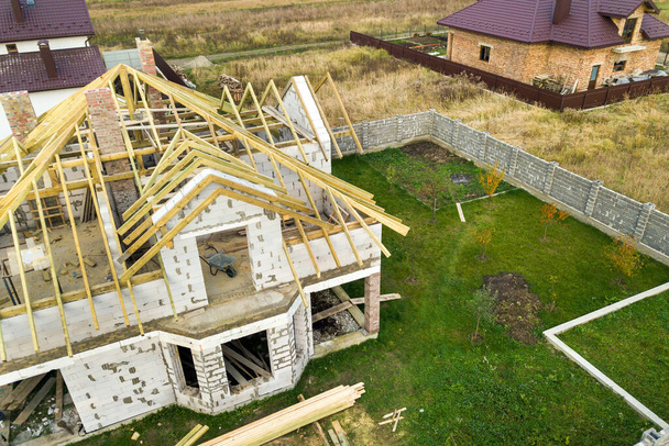 Вид с воздуха на частный дом с кирпичными стенами из газобетона и деревянной рамой для будущей крыши. - Фото, изображение