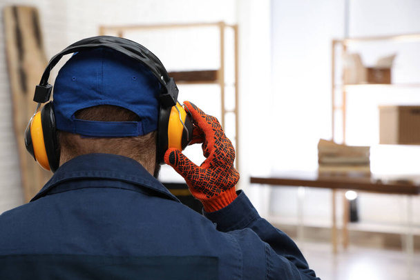 Werknemer draagt een veiligheidshoofdtelefoon binnen, achteraanzicht. Gehoorbeschermingsinrichting - Foto, afbeelding