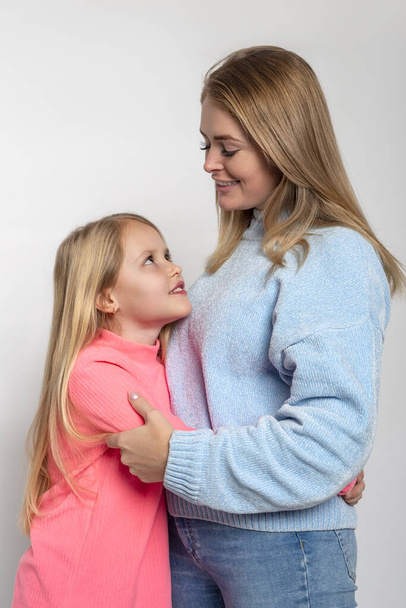 Half length portrait  of happy cheerful mom and daughter looking at each other with tenderness on a white background in the studio - Photo, Image