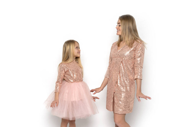 Напівдовжина портрет привабливої маленької дівчинки з мамою в рожевих сукнях дивиться один на одного на білому тлі в студії
 - Фото, зображення