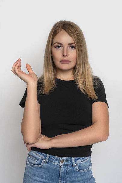 Nahaufnahme Porträt eines attraktiven blonden Mädchens in schwarzem Hemd und Jeans, das vor grauem Hintergrund im Studio posiert - Foto, Bild