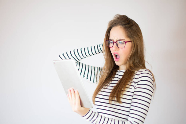 Chica joven sorprendida usando tableta digital sobre fondo blanco, espacio de copia - Foto, imagen