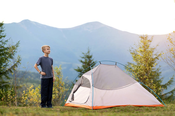 Heureux enfant garçon debout près d'une tente touristique au camping de montagne bénéficiant d'une vue sur la belle nature estivale. Concept de randonnée et mode de vie actif. - Photo, image