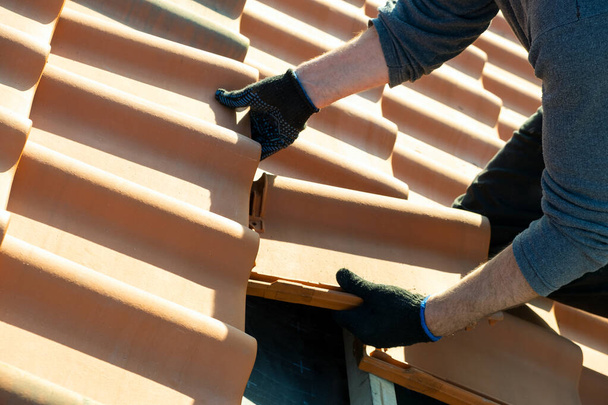 木造建築物の屋根を覆う板に取り付けられた黄色のセラミック屋根瓦を建設中の労働者の手の閉鎖. - 写真・画像