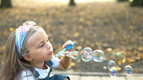 緑の公園の外でシャボン玉を吹いている小さな幸せな子供の女の子。アウトドア夏のアクティビティコンセプト. - 写真・画像