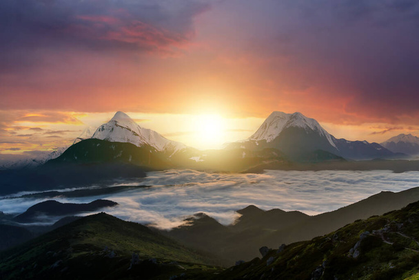 Ηλιοβασίλεμα τοπίο με υψηλές κορυφές και ομιχλώδη κοιλάδα με παχιά λευκά σύννεφα κάτω από ζωντανό πολύχρωμο ουρανό βράδυ σε βραχώδη βουνά. - Φωτογραφία, εικόνα