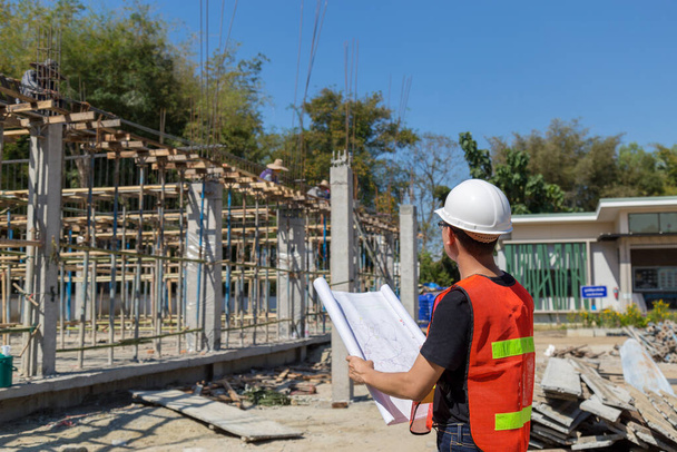 Ingenieure tragen einen Helm und halten einen Bauplan in der Hand, der das Baugebiet überwacht. - Foto, Bild