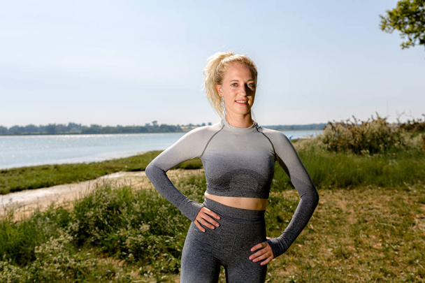 Attraktive, fitte junge Frau in Sportkleidung, die bereit ist, in der Sonne am Ufer des Flusses zu trainieren. Gesunder Lebensstil - Foto, Bild