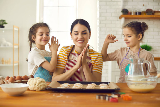 Happy young woman and her cute little daughters making sweet yummy cookies at home - Photo, Image