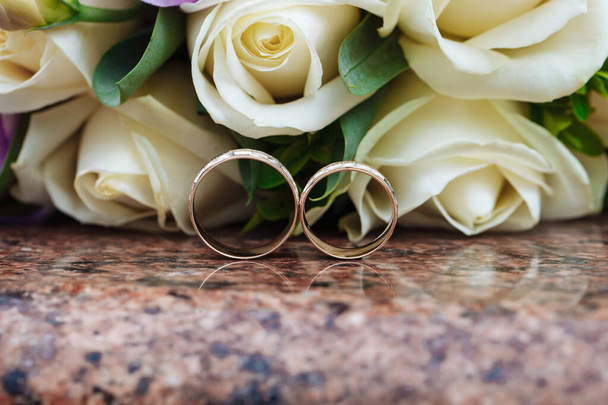 Svatební prsteny na žulovém stojanu na pozadí krásné kytice květin - Fotografie, Obrázek
