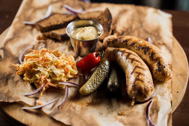 Grillwürste mit Bier und Gemüse mit eingelegter Gurke, Kohlsalatsoße und Brot auf Pergament, von oben. - Foto, Bild