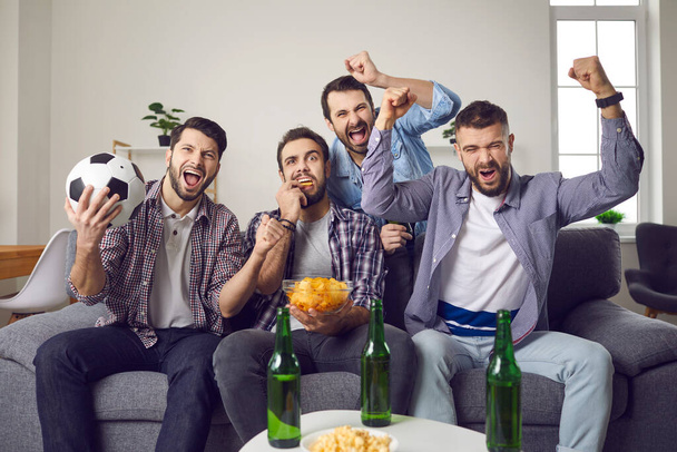 Male friends celebrating favourite teams goal during watching football television match - Foto, afbeelding