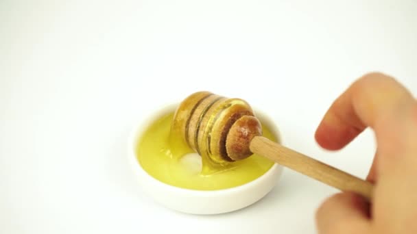 Miel líquida tomando con palo de madera de plato blanco pequeño - Imágenes, Vídeo