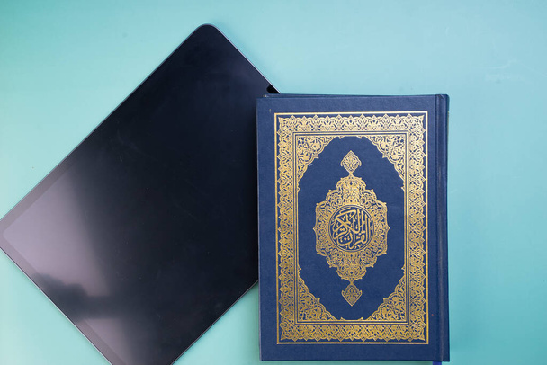 Η εφαρμογή τεχνολογικών συσκευών και εφαρμογών στην ψηφιοποίηση του Κορανίου, ή e-Quran. Online μάθηση, ή Quran ρεσιτάλ χρησιμοποιώντας εφαρμογές. Οι αραβικές λέξεις στο βιβλίο σημαίνουν Ιερό Κοράνι - Φωτογραφία, εικόνα