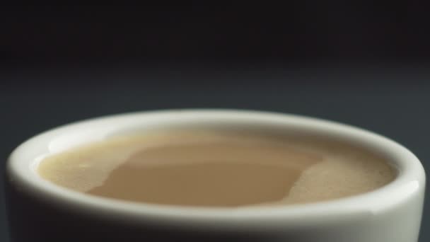 Slow motion macro shot of coffee drop falling from the coffee machine into white κεραμικά κούπα γεμάτη με φρέσκο καφέ σε μαύρο φόντο. Crema για καφέ. Μια σταγόνα αναπηδά σε αργή κίνηση 100fps - Πλάνα, βίντεο