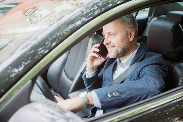Handsome caucasian businessman driver inside in vehicle and gadget and check mail and talking with partners - Fotografie, Obrázek