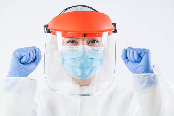 Healthcare professional in personal protective equipment, wearing surgical gloves, face shield, white protective hazmat biohazard suit, clenched fists raised in air and smile,happy and victorious - Photo, Image