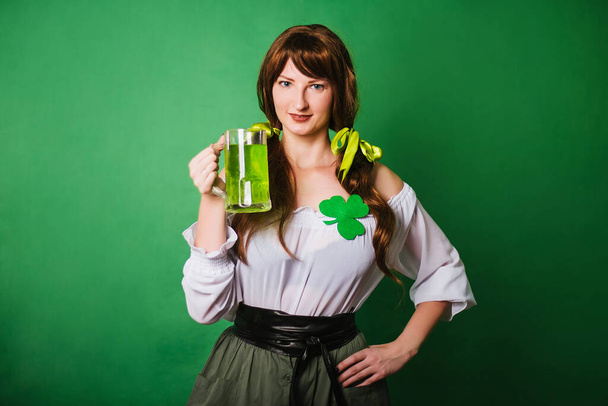 La fille célèbre la Saint Patrick. Une femme en costume historique médiéval avec une grande tasse de bière verte. L'image d'une paysanne - Photo, image