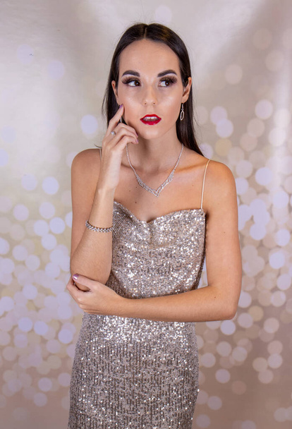 A sexy elegant woman wearing a silver glittery party dress with long brown hair and red lipstick and a diamond necklace looking like she is ready for an elegant Christmas party or wedding event - Photo, Image