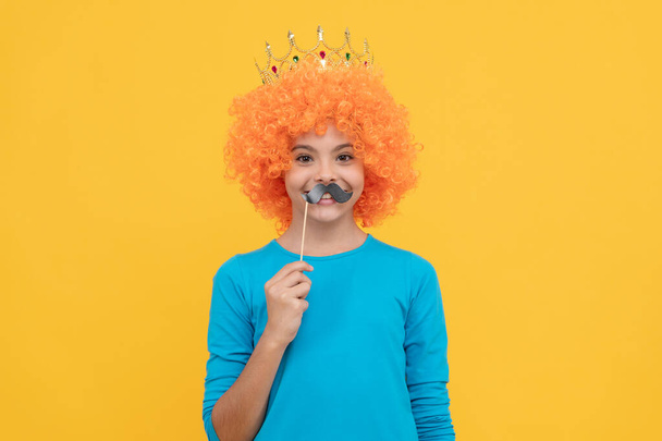 Şık palyaço peruğu takan mutlu genç kız kraliçe tacı ve komik parti bıyığı takıyor, 1 Nisan. - Fotoğraf, Görsel