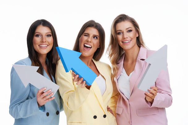 Drie vrouwen in pastel pakken poseren met pijlen over witte achtergrond - Foto, afbeelding