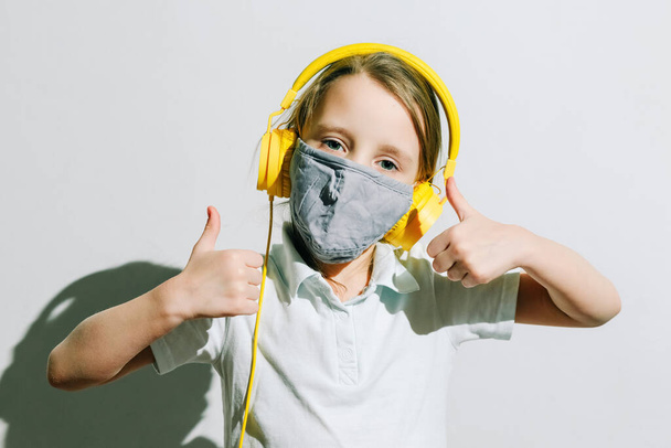Girl in a medical mask and yellow headphones, good mood and optimism - Fotoğraf, Görsel
