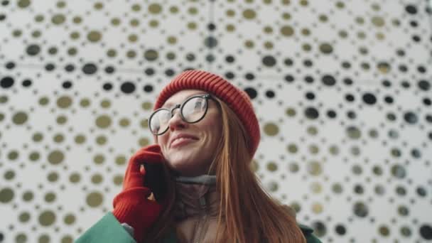 Niski kąt ujęcia młodej atrakcyjnej kobiety stojącej na zewnątrz w pobliżu budynku miejskiego w zimowy dzień i rozmawiającej przez telefon komórkowy - Materiał filmowy, wideo