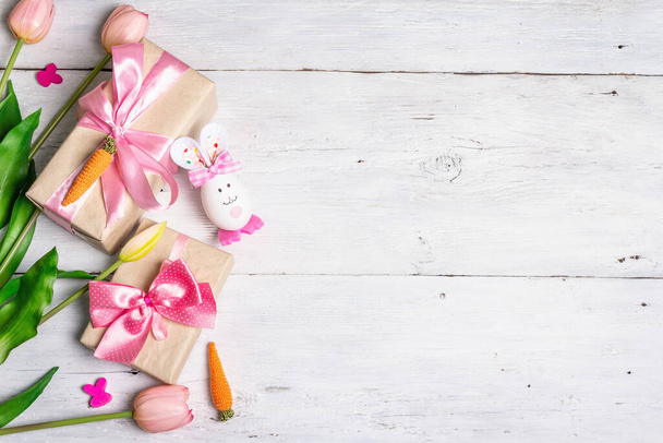 Tradiční koncept velikonočních symbolů. Roztomilý králík z vajíčka, dárková krabice, slavnostní dekor v růžových tónech. Bílé dřevěné pozadí, horní pohled - Fotografie, Obrázek