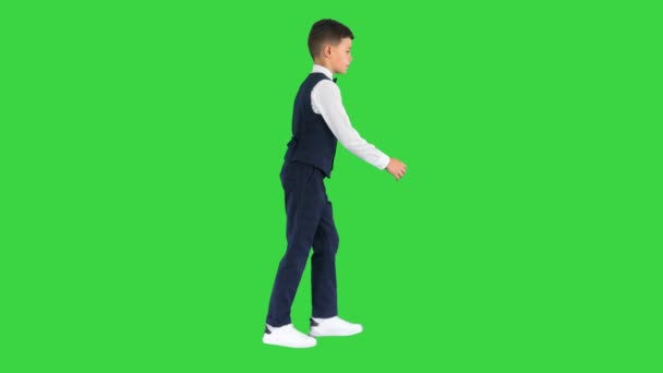 Egy kisfiú csokornyakkendőben és mellényben, aki egy zöld vásznon lóbálja a kezét, Chroma Key.. - Felvétel, videó