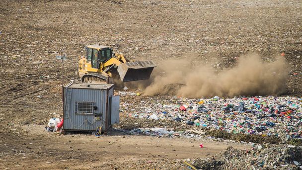 Żółty traktor rozładowujący odpady na ogromnym wysypisku dużych miast. Dużo śmieci na wysypisku. Sortowanie odpadów. - Zdjęcie, obraz
