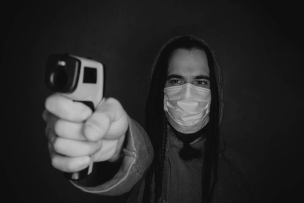 Young man posing with infrared forehead thermometer gun over dark background - Foto, Imagen