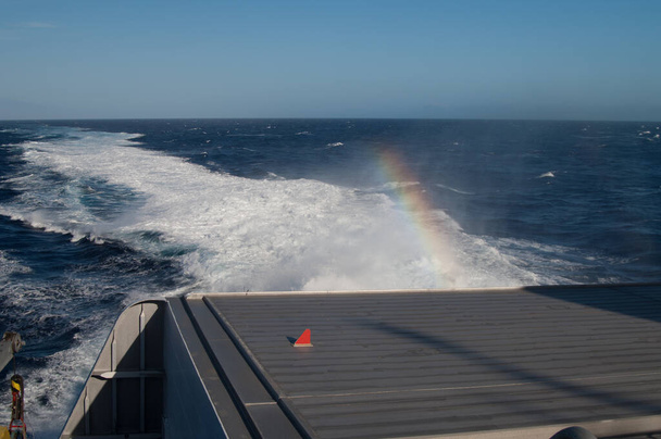 Achterzijde van een schip, wake en regenboog. - Foto, afbeelding