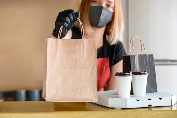 Food bag, pizza, drink package to go in takeaway restaurant. Kitchen worker issues online orders in gloves and mask. Takeaway food paper bag mock up. Contactless food delivery lockdown covid 19. - Fotoğraf, Görsel