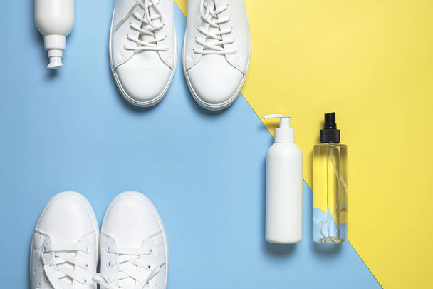 White leather sneakers, plastic bottles of cleaning products for shoes on blue yellow background flat lay top view. Natural leather shoe care, spray, foam, shoe deodorant, cosmetic shoe products. - Photo, Image
