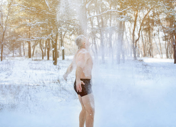 Cold weather training, winter fun. Mature man in underwear standing under falling snow, throwing it at himself in park - Photo, Image