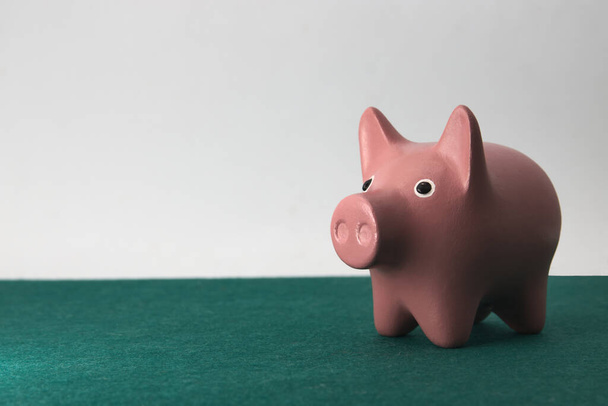 Image of a pink piggy bank on a green table and neutral background with copy space - Zdjęcie, obraz