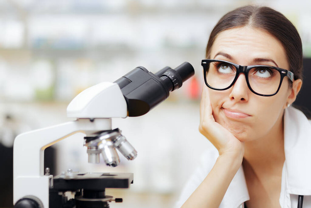 Unhappy Scientist Looking through a Microscope in a Laboratory - Foto, afbeelding