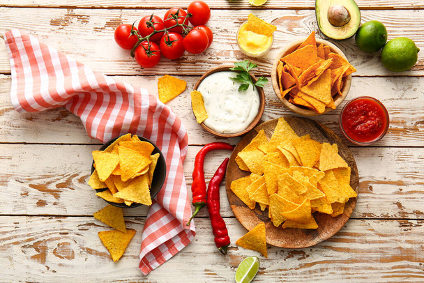 Plates with tasty nachos and sauces on light wooden background - Fotografie, Obrázek