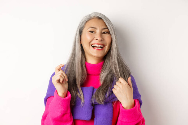 Close-up de moda asiática mulher sênior, rindo e se divertindo, olhando para a esquerda alegre, de pé sobre fundo branco - Foto, Imagem