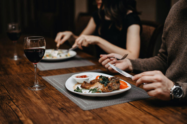 Un homme et une femme déjeunent dans un restaurant. Nourriture et vin rouge. Mise en table. Les mains tiennent le vidku et le couteau sur la plaque - Photo, image