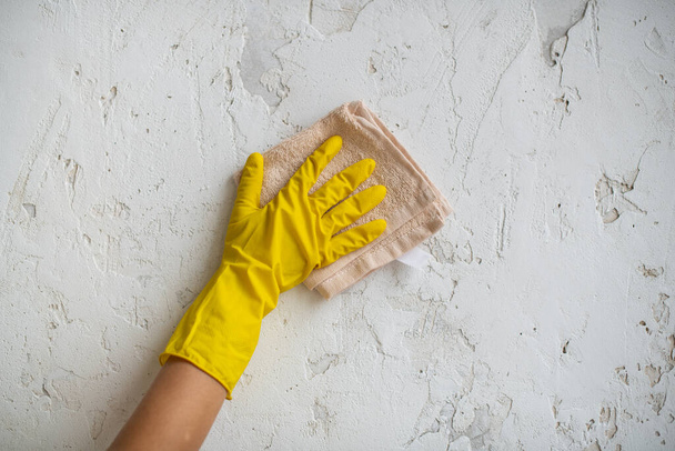 Уборка территории, уборка. Гигиена и чистота на кухне. Уборщица в жёлтой резиновой перчатке вытирает пыль со стены. Рабочая рука - Фото, изображение