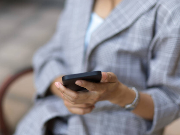 Nahaufnahme einer Geschäftsfrau, die ihr Smartphone in der Hand hält, während sie sich im Café entspannt - Foto, Bild