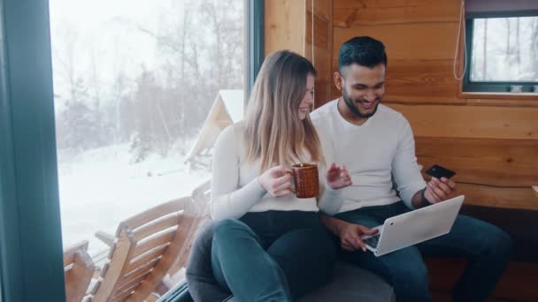 Счастливая молодая многорасовая пара, использующая кредитку для покупок в интернете. Бронирование зимних каникул - Кадры, видео